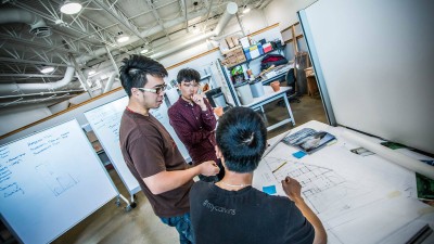 Architecture students discuss sketch at a desk.