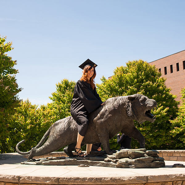 An RIT grad sitting on the Tiger Statue