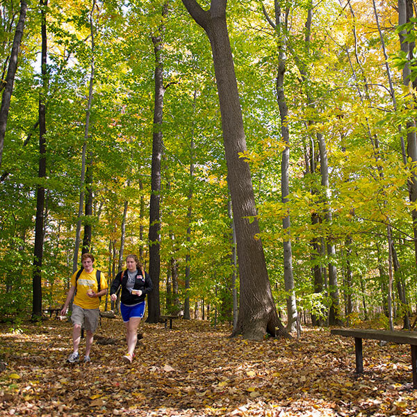 Two RIT students walking on a trail through the woods