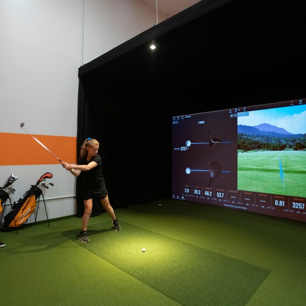 A student hitting a golf ball in the Golf Simulator at the Student Life Center 
