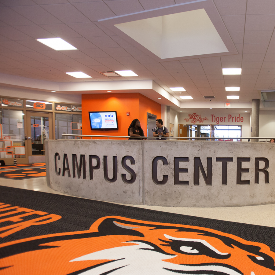 Two student leaning against a campus center sign with the campus center lobby.