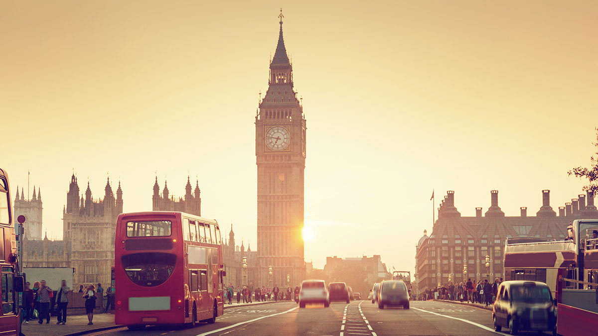 Big Ben and Westminster at sunset with red double-decker buses and cars on a busy London street.