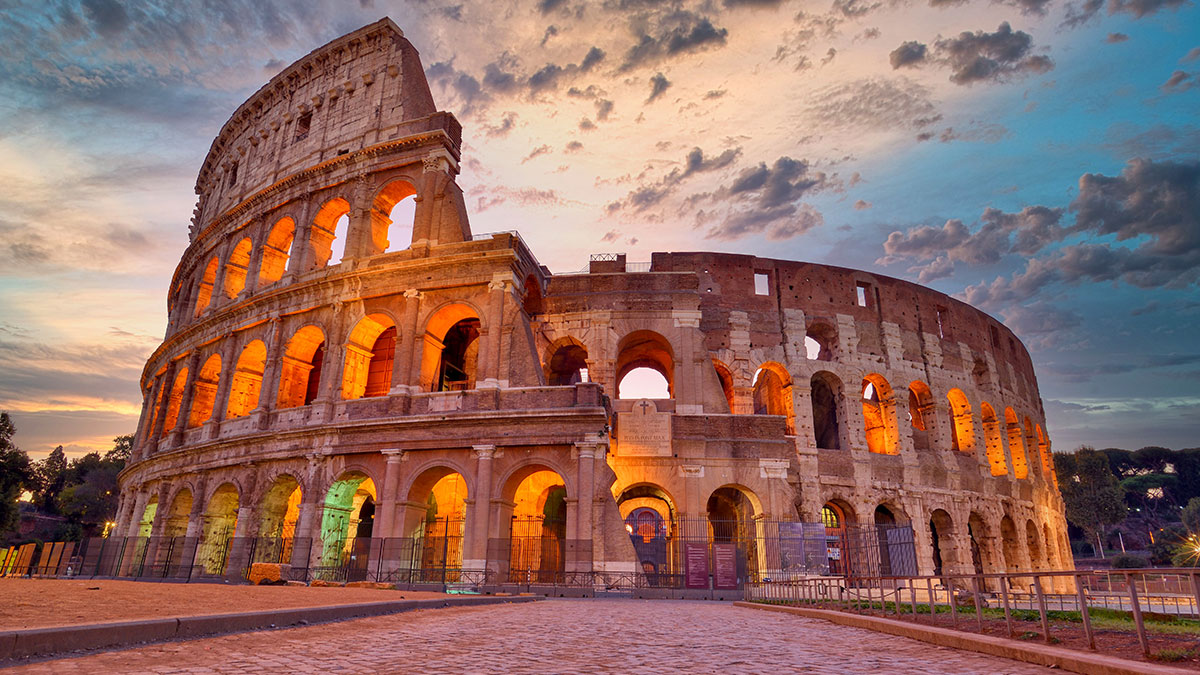 The Colosseum in Rome, Italy, illuminated at dusk under a dramatic sky with colorful clouds.