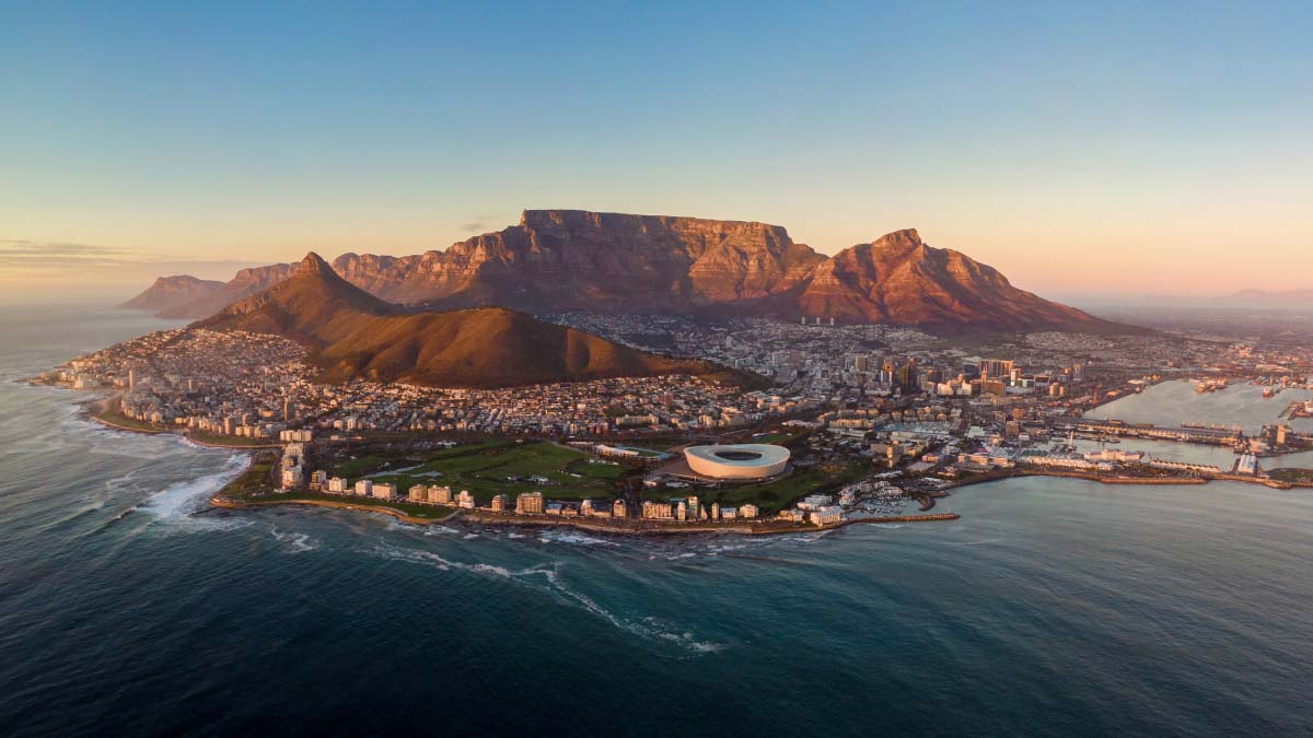 Aerial view of Cape Town at sunset, with Table Mountain rising behind the stadium and coastline.