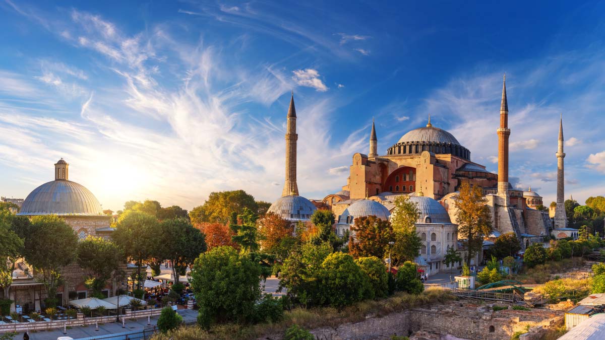 Hagia Sophia's domes and minarets rise above trees and rooftops in Istanbul at golden hour.