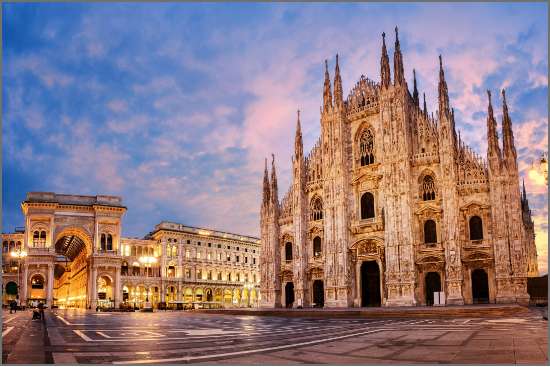 The Duomo Cathedral in Milan, Italy, illuminated at sunset with intricate Gothic architecture and a glowing sky in the background.