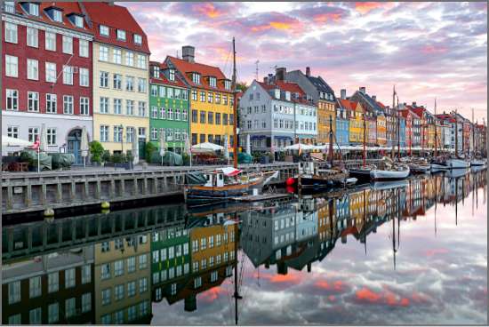 Colorful buildings line the Nyhavn canal in Copenhagen, with boats and vibrant reflections mirrored in calm water at sunset.
