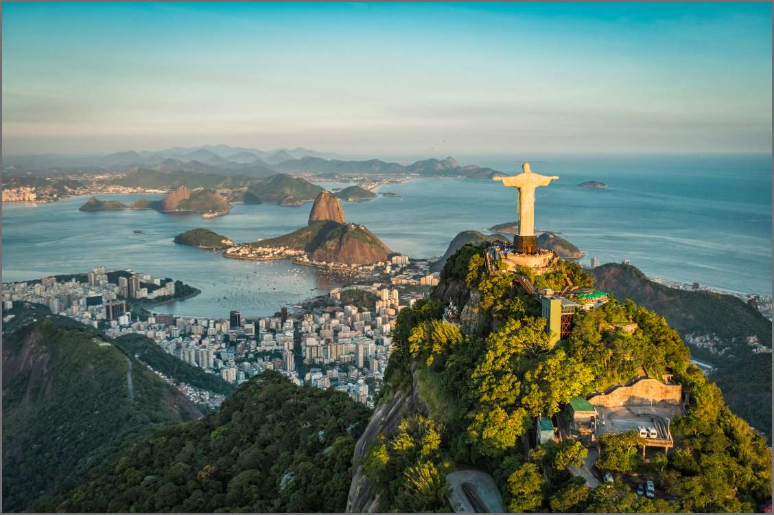 A stunning aerial view of Rio de Janeiro, Brazil, featuring the Christ the Redeemer statue overlooking the city, bay, and lush green mountains.