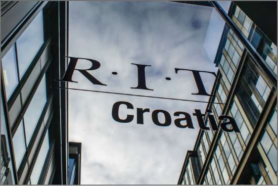 RIT Croatia logo displayed on a modern glass building reflecting the sky and surrounding architecture.