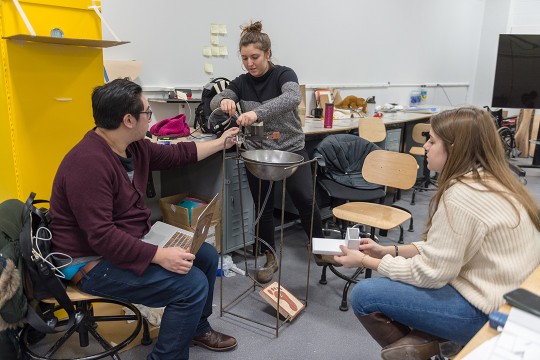 one student stands and two students sit around prototype of simple sink