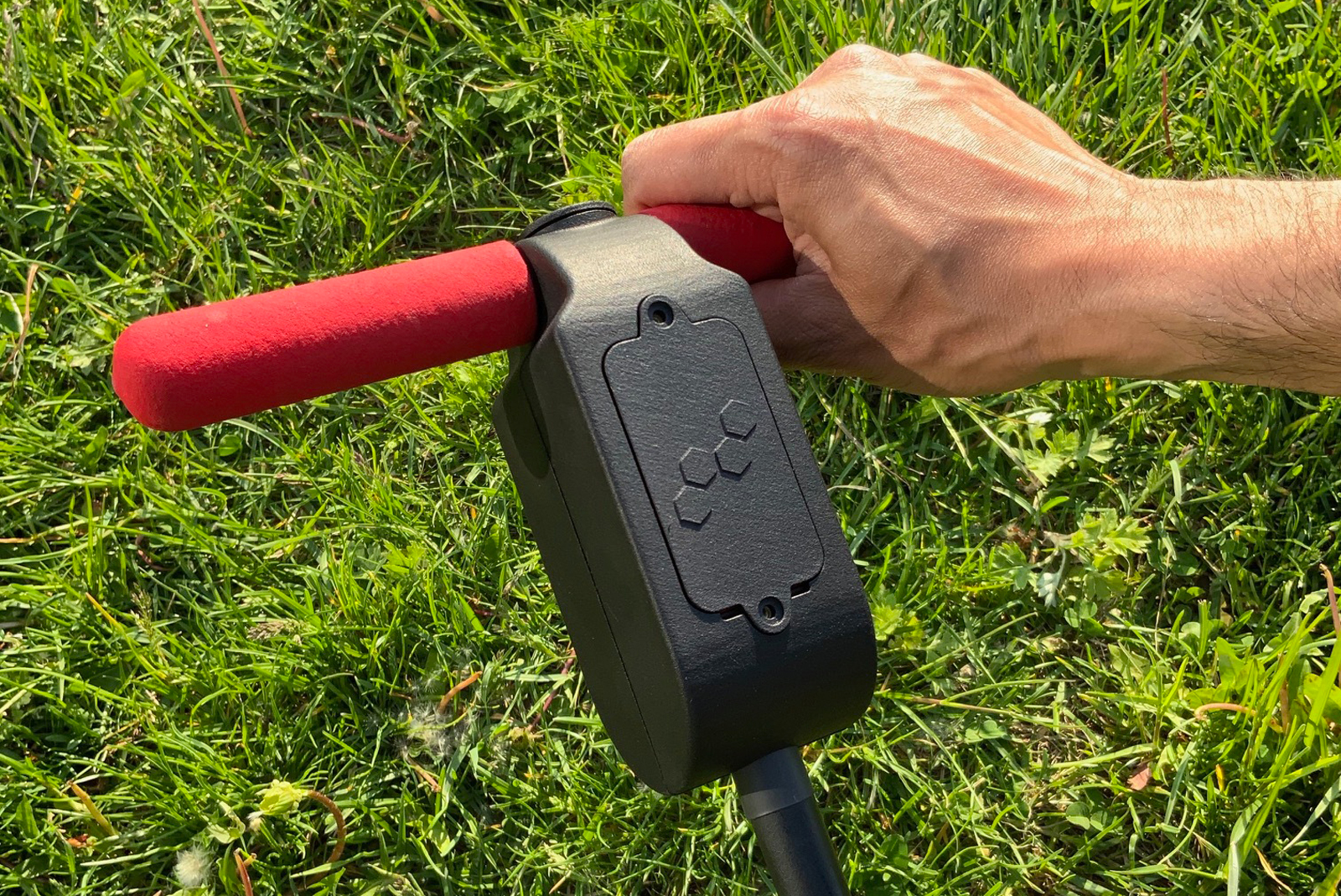Hand holding a Smart Sensor Compost System over a bed of grass