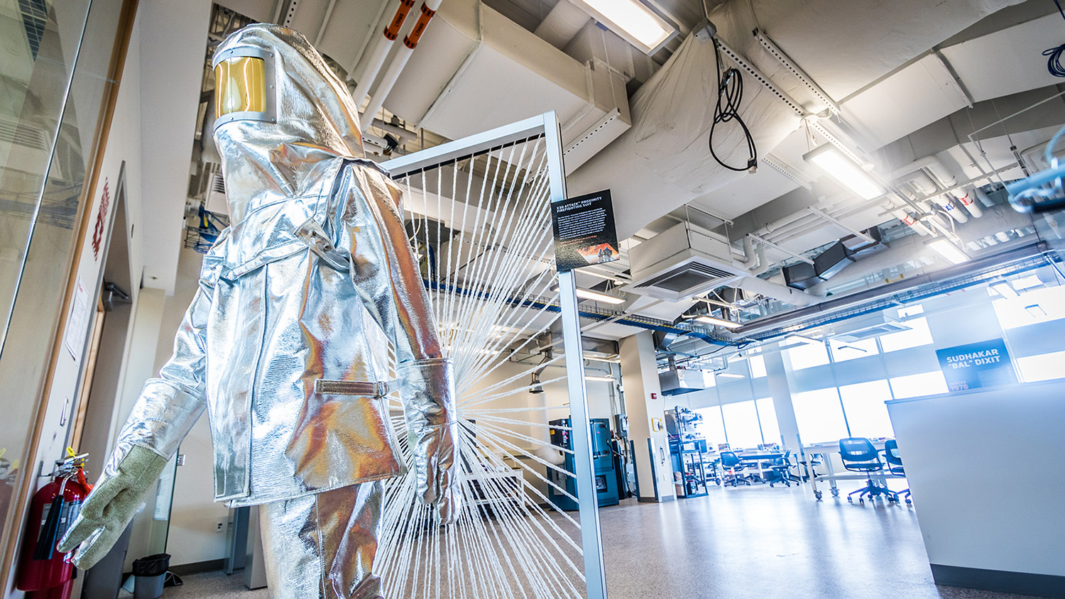 mannequin in foreground wearing silver heat protection suit with lab in background