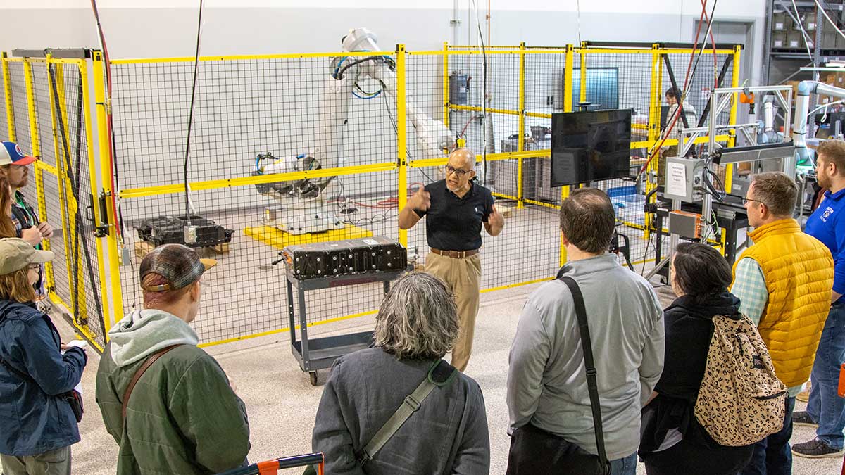 A group of people observing a demonstration of industrial robotics in a testing facility.
