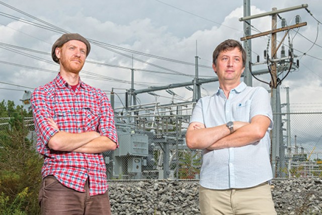 Eric Hittinger and Eric Williams post for a photo together in front of powerlines, both of their arms crossed.