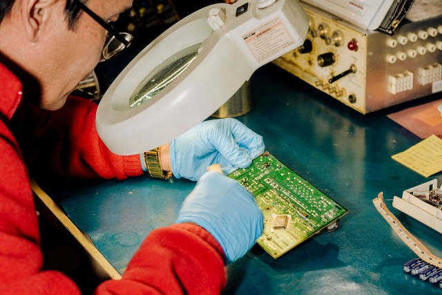 worker looking at circuit board with lighted magnifier.