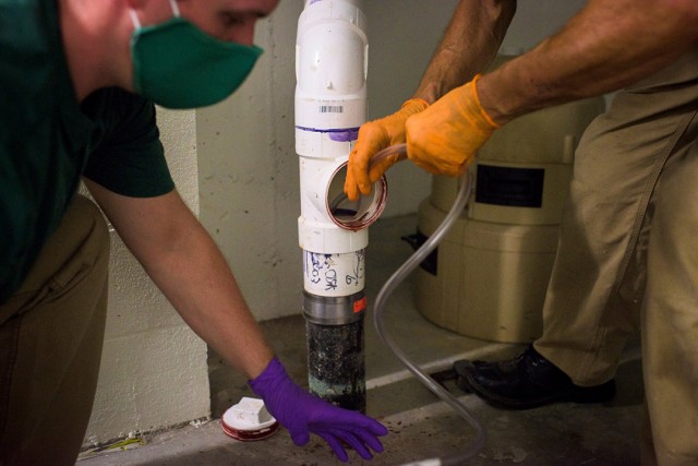 two workers taking sample of wastewater from pipe.