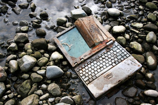old, dirty laptop sitting in a riverbed.