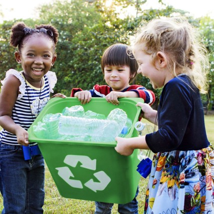 three children holding a recycling bin full of plastic waterbottles.