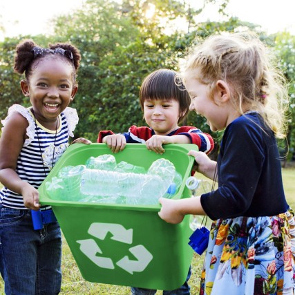 three children holding a recycling bin full of plastic waterbottles.