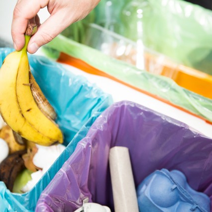 person throwing away a banana peel into a container with other food waste.