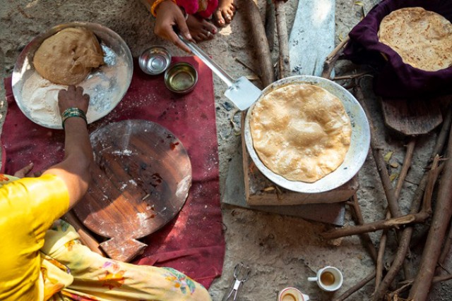 a variety of traditional indian foods, like naan bread, are shown in pans from above.