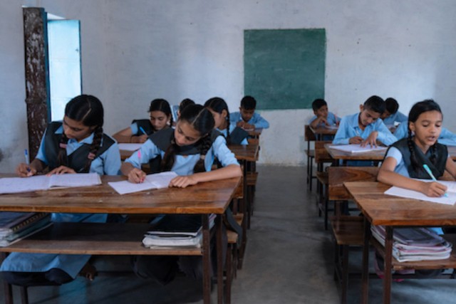 students sit working at desks in a rural classroom in india