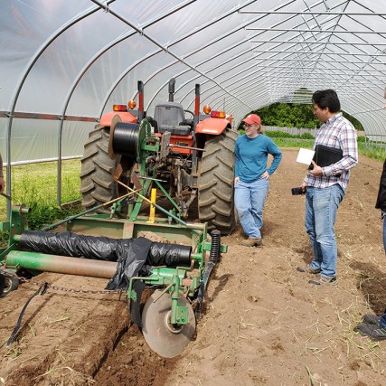 farmers and researchers in greenhouse using tractor to put down mulch barrier.