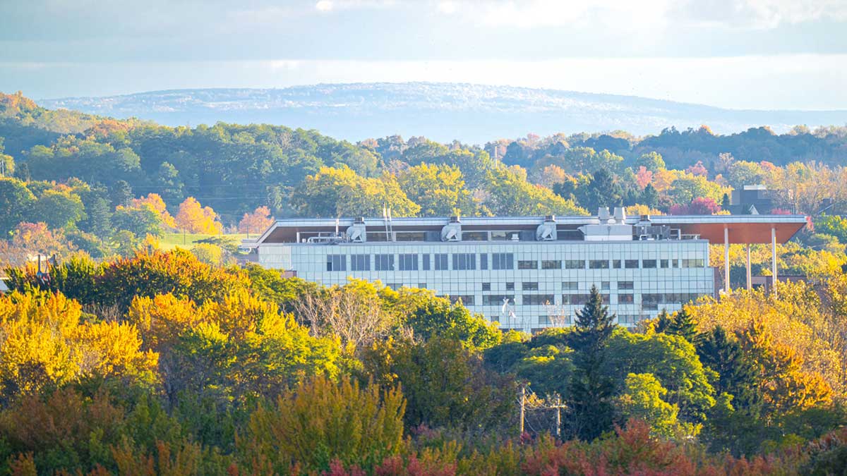 A modern campus building is surrounded by colorful autumn foliage with distant hills in the background.