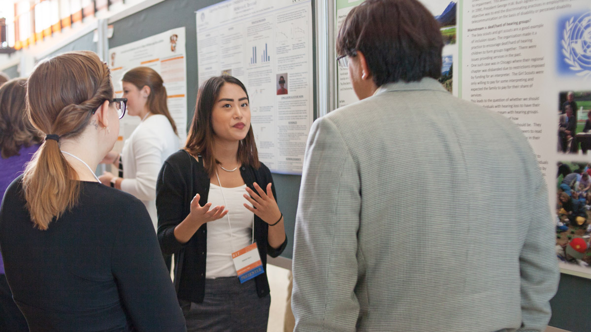 A student presents their research to onlookers.