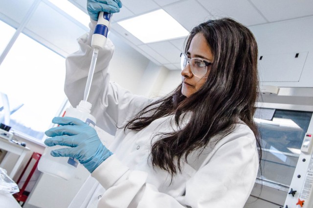 Woman in goggles and lab coat, squeezing a liquid in a bottle.