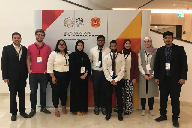 A group of RIT Dubai mechanical engineering students pose in front of a poster for the Expo.