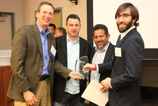 four people holding award together.