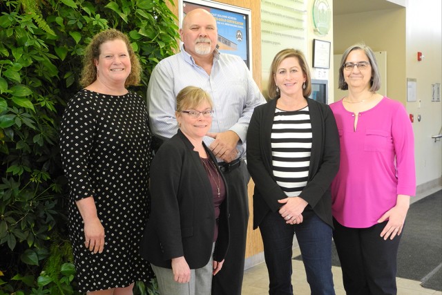 Group of faculty members stand near wall of plants