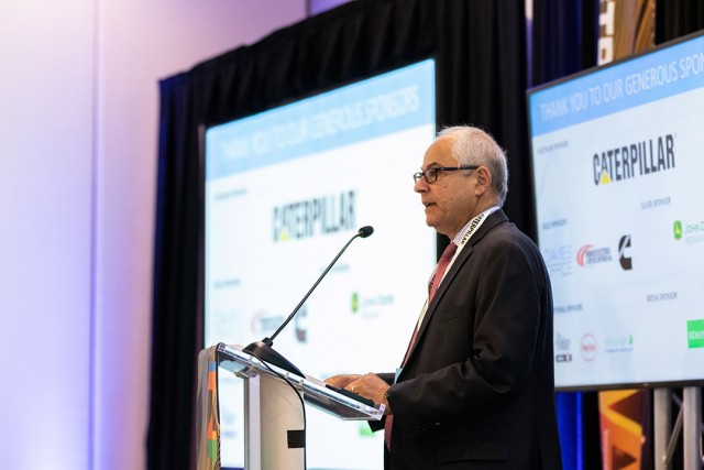 Nabil Nasr presents in front of projector and TV screens.