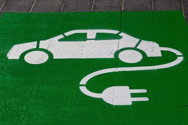 icon of a car with a cord and plug spraypainted onto a roadway.