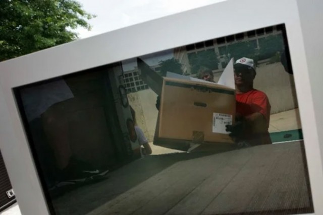TV screen showing reflection of man loading box into truck.