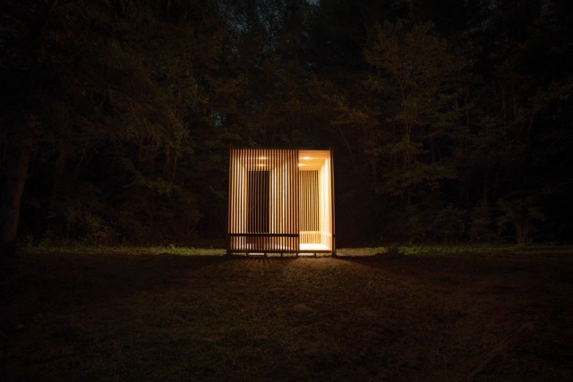 A wooden structure is illuminated at night amongst trees.