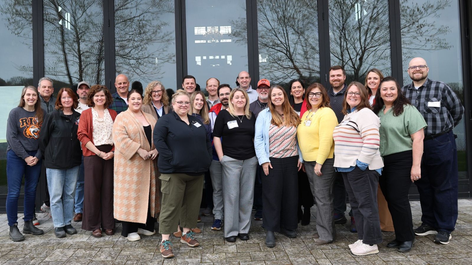 twentyfive people standing in front of a glass wall posing for a group photo