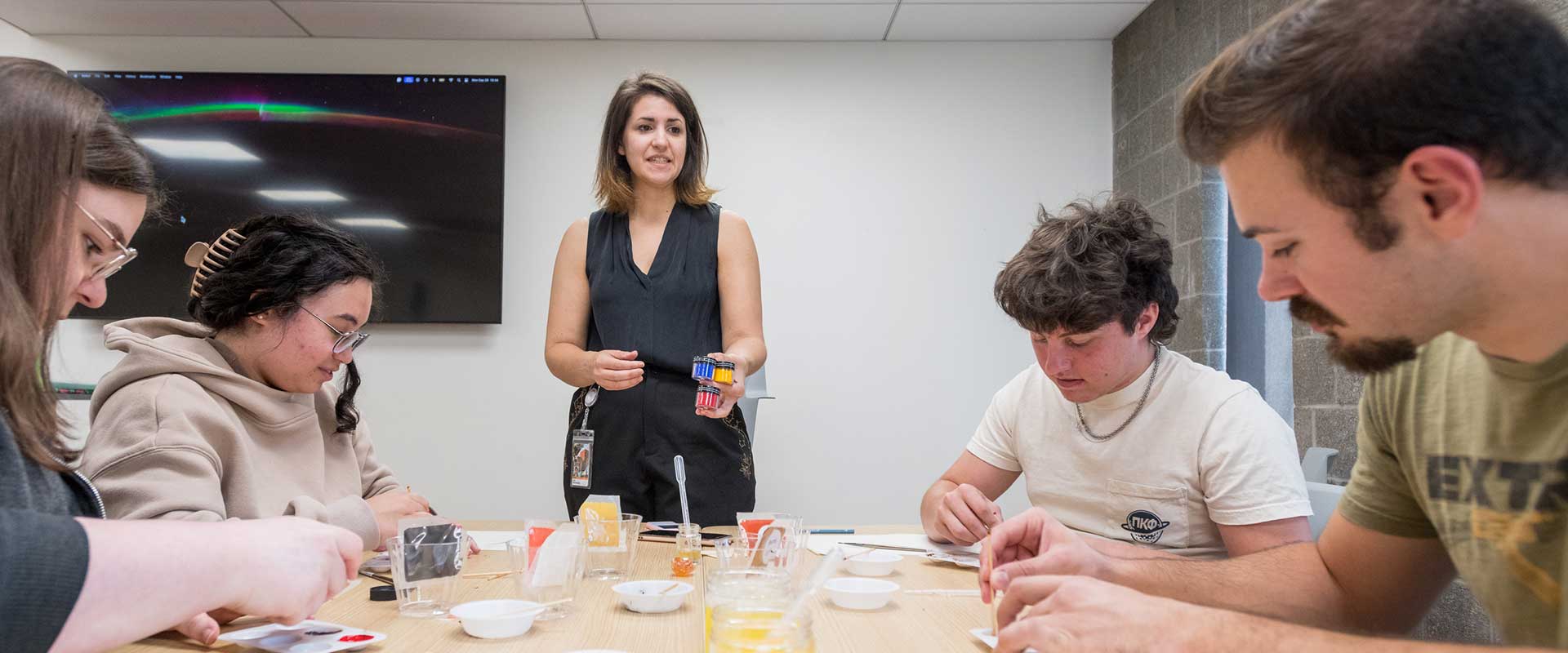 Instructor speaking to students, students seated around a table