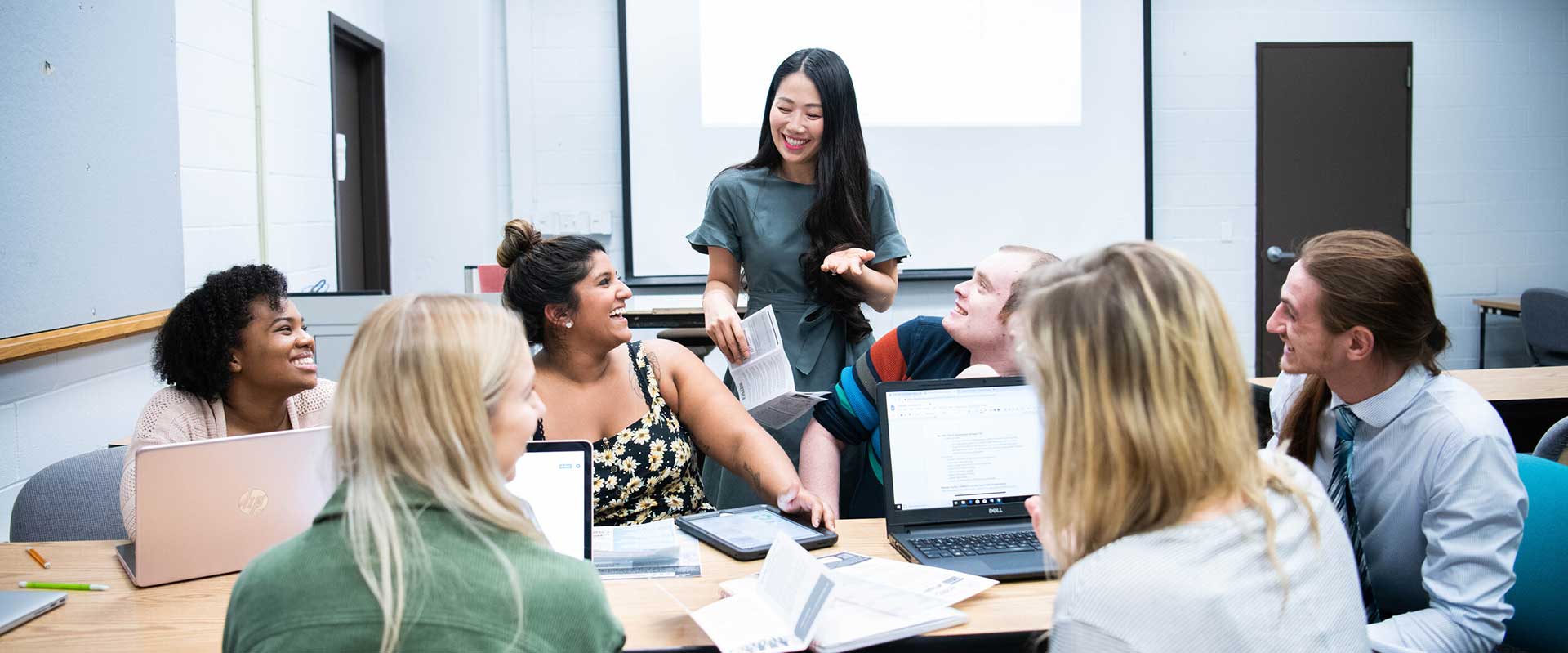 Instructor standing in a classroom speaking to a group of seated students