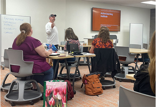 Faculty standing at the front of room presenting with a few faculty members seated