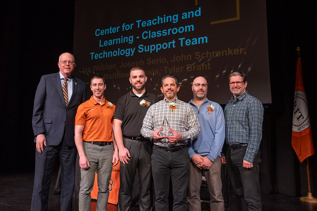Center for Teaching and Learning team poses on stage with an award in front of a projection screen.