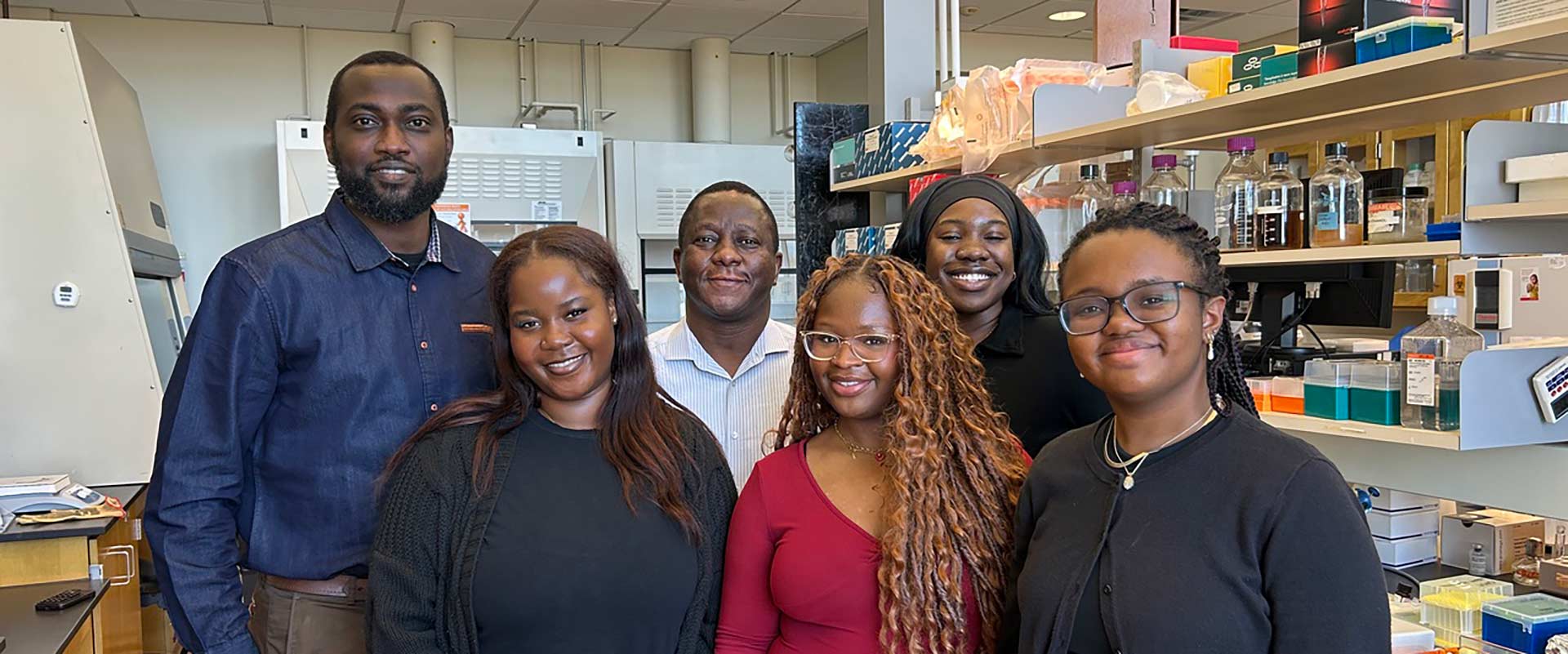 professor stands with five students in a lab setting.