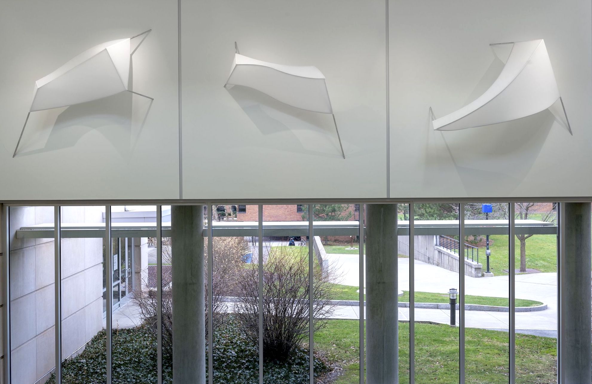 Installation of three sculptural forms made of white fabric stretched over a 3D armature and mounted on the wall.
