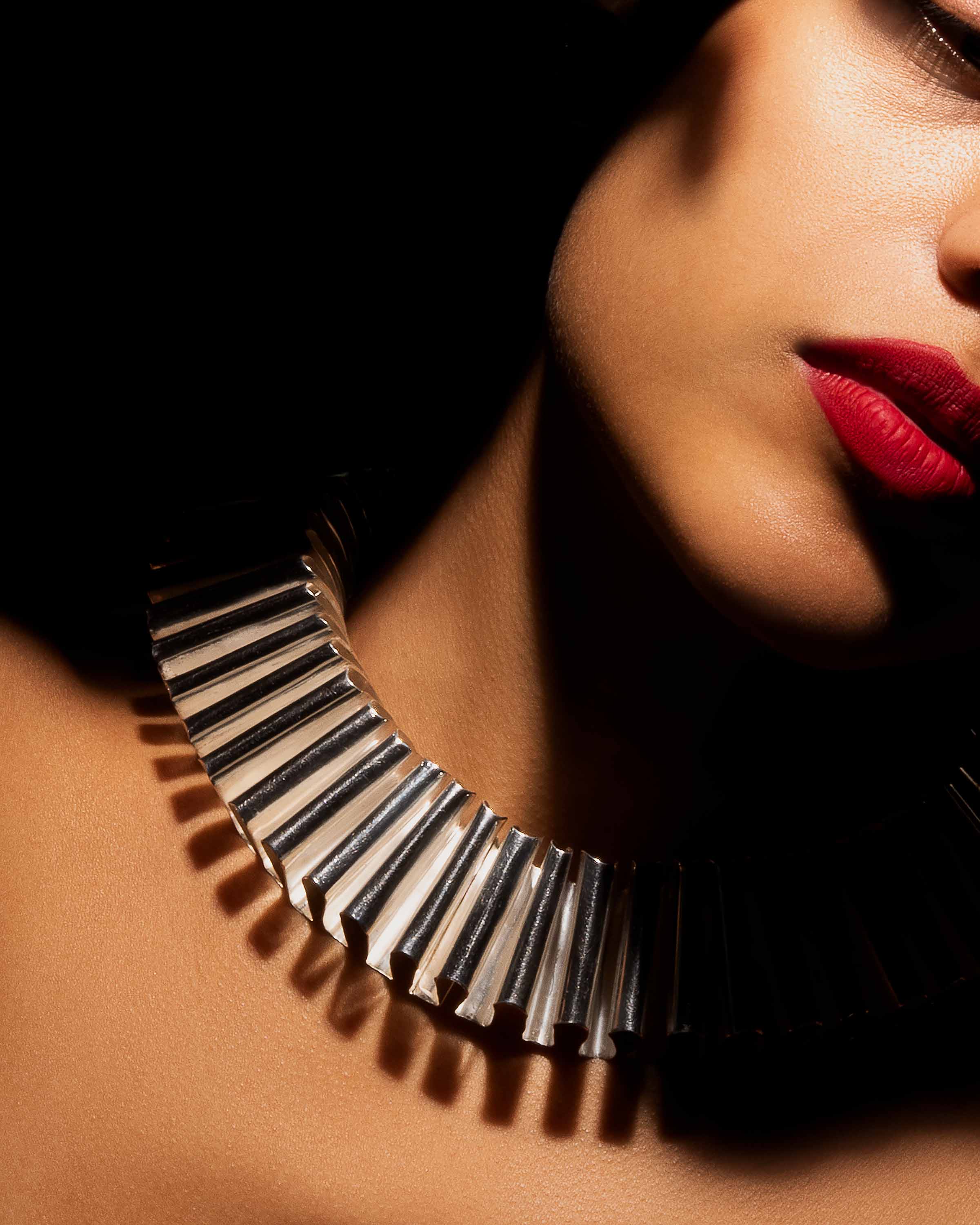 a photographic close up of a woman's face tilting to the side with a large silver necklace. 