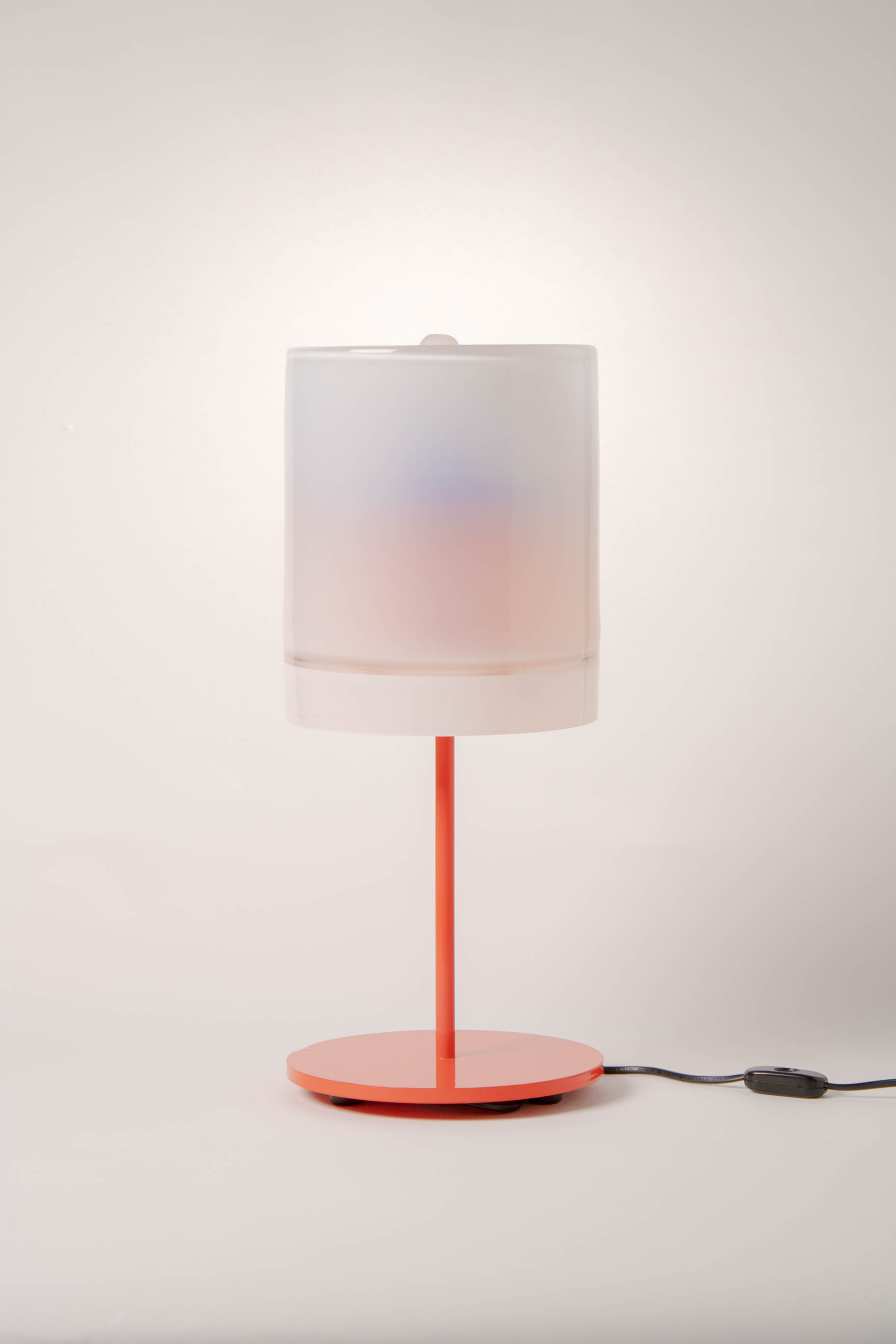 a lamp with a red metal base and white cylindrical shade against a white background.