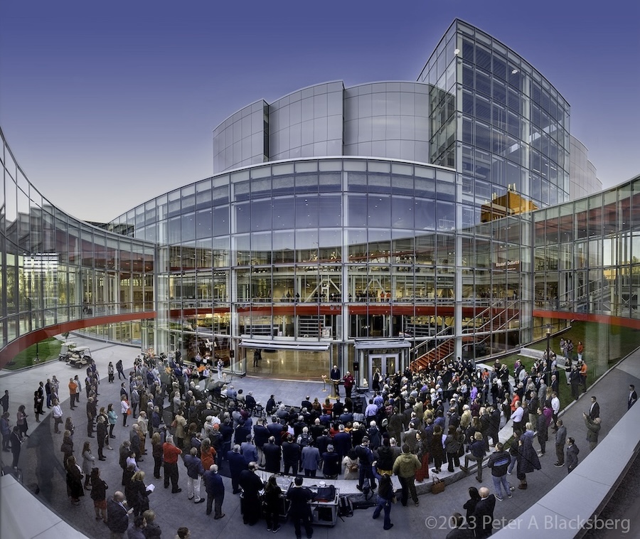 a panoramic color photograph of a ribbon cutting ceremony in front of a soaring glass and steel building.