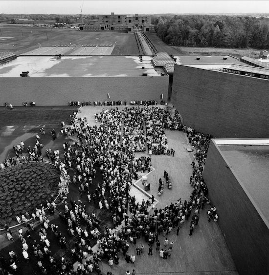 a black and white aerial photograph with a view on building rooftops and a large cloud of people gathered for an event.
