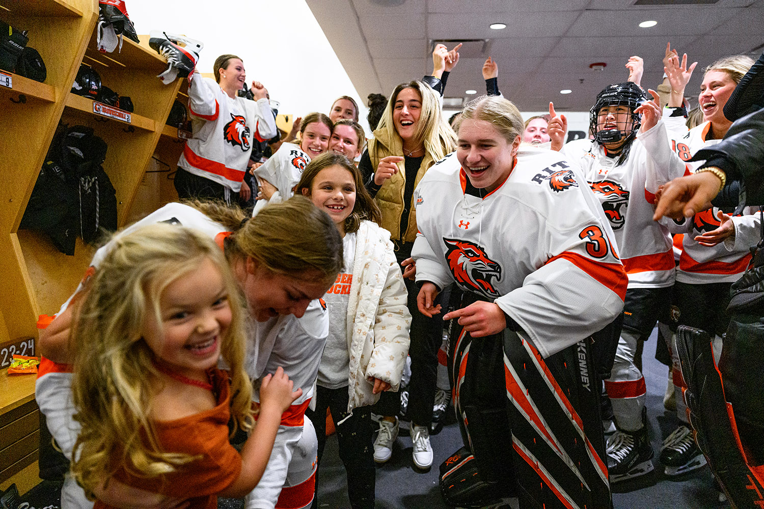 a color photograph of a women's ice hockey team in full uniforms in a locker room celebrating a win.