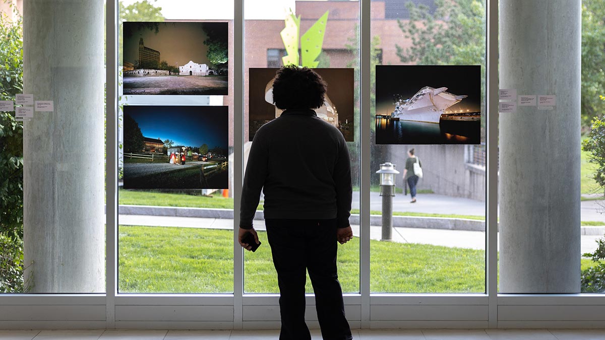 a student looking at artwork hanging from tall windows.